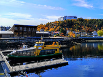 Marina au Saguenay avec petit bateau de croisière sur fond d'arbres aux couleurs automnales.