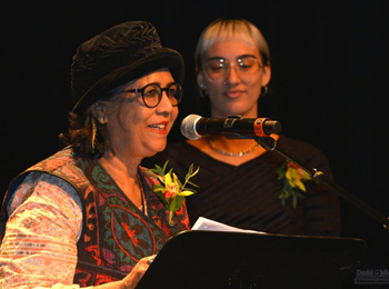 Une femme qui devant un micro et un podium récite un poem et une jeune femme se tient à côté d'elle.