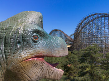Gros plan sur la tête d'un dinosaure, avec une montagne russe en arrière-plan.