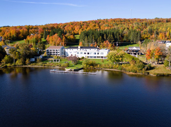 Le Manoir Lac-Etchemin au bord du lac avec les arbres aux couleurs automnales derrière.