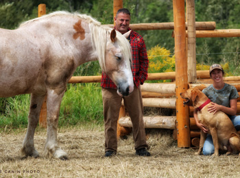 Un homme se tient à côté d'un cheval, et près de lui, une femme est accroupie avec un chien.