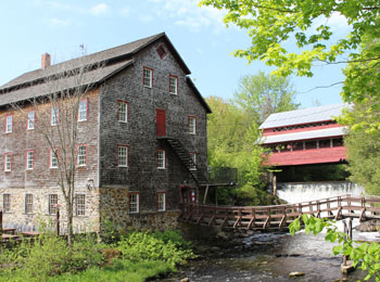 Extérieur du bâtiment ancestral, avec un petit pont en bois qui surplombe un ruisseau.