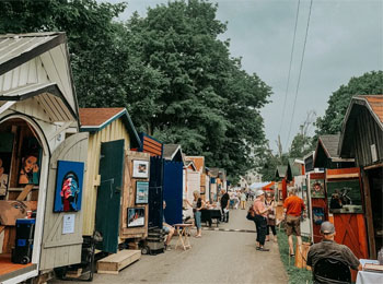 Ruelle bordée de petites cabanes dans lesquelles sont exposées des oeuvres d'art.