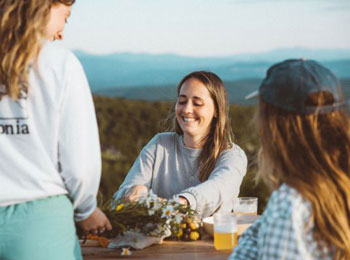 Trois jeunes femmes autour d'une table, avec les montagnes en arrière-plan.